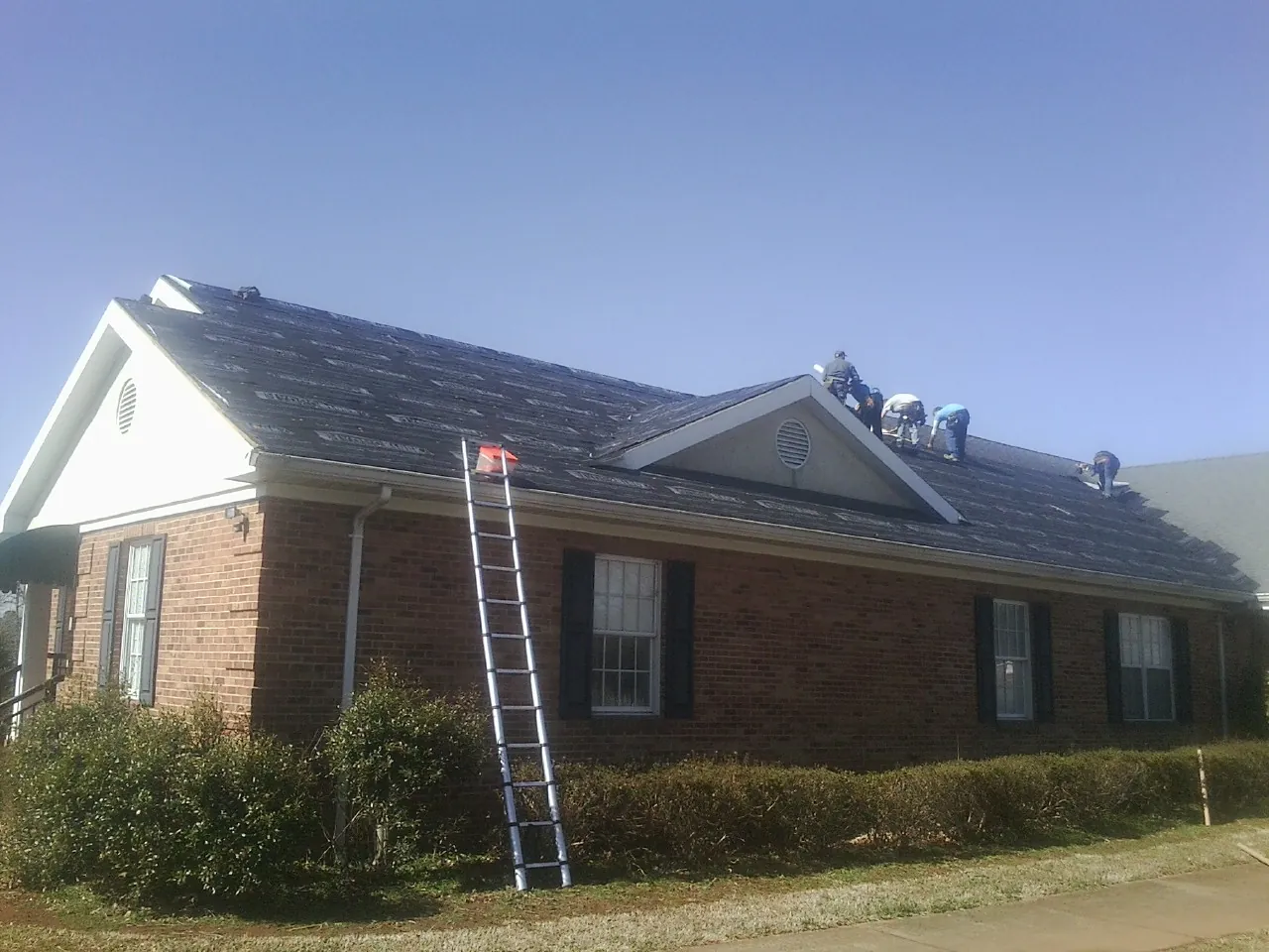 Crew tearing shingles off a brick ranch roof with a ladder set — Emergency Roof Repair work by our crew in Belcamp