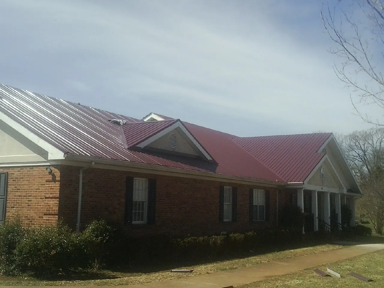 Red metal roof with gabled entries on a long brick building, from a Hail Damage Roof Repair job in Belcamp