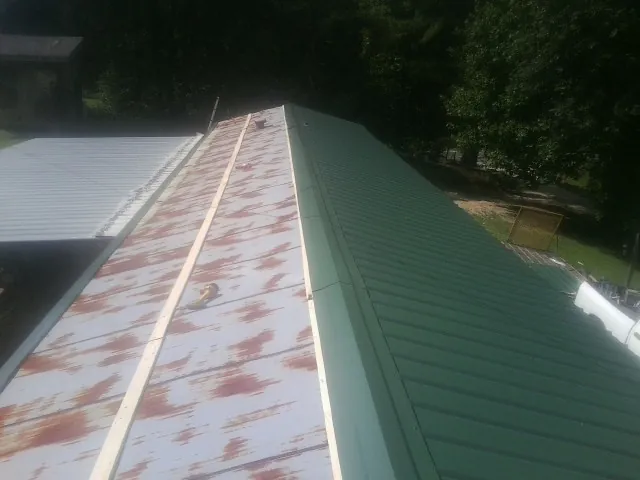 Old rusted panels beside newly installed green metal roofing — Wind Damage Roof Repair by Roofing Brothers in Belcamp