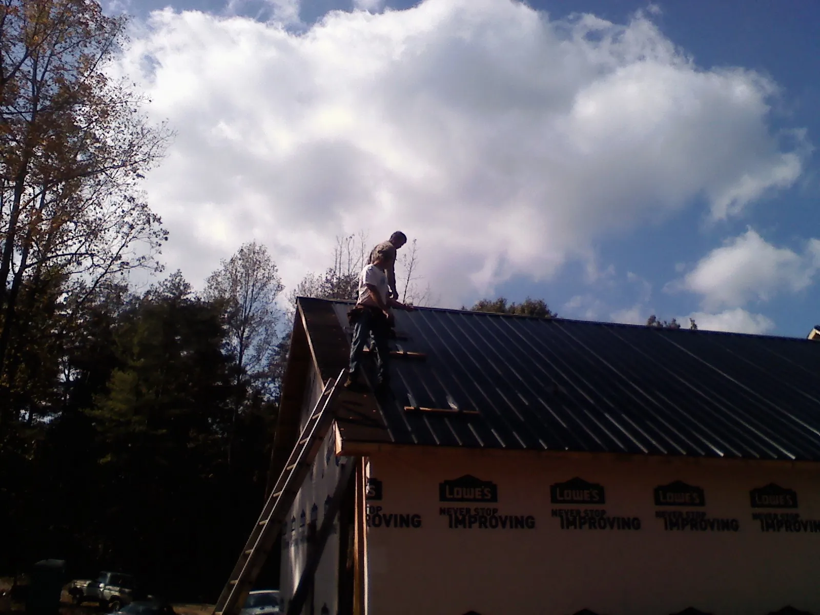 Roofer fastening dark metal panels high against a cloudy sky, from a Roof Inspection job in Belcamp