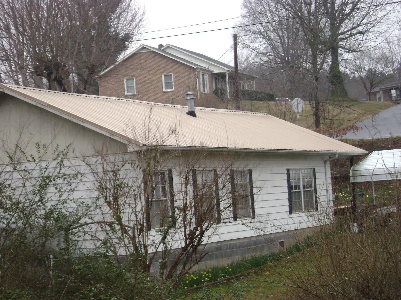 Tan metal roof on a white sided house set into a hillside — Commercial Roofing by Roofing Brothers in Belcamp